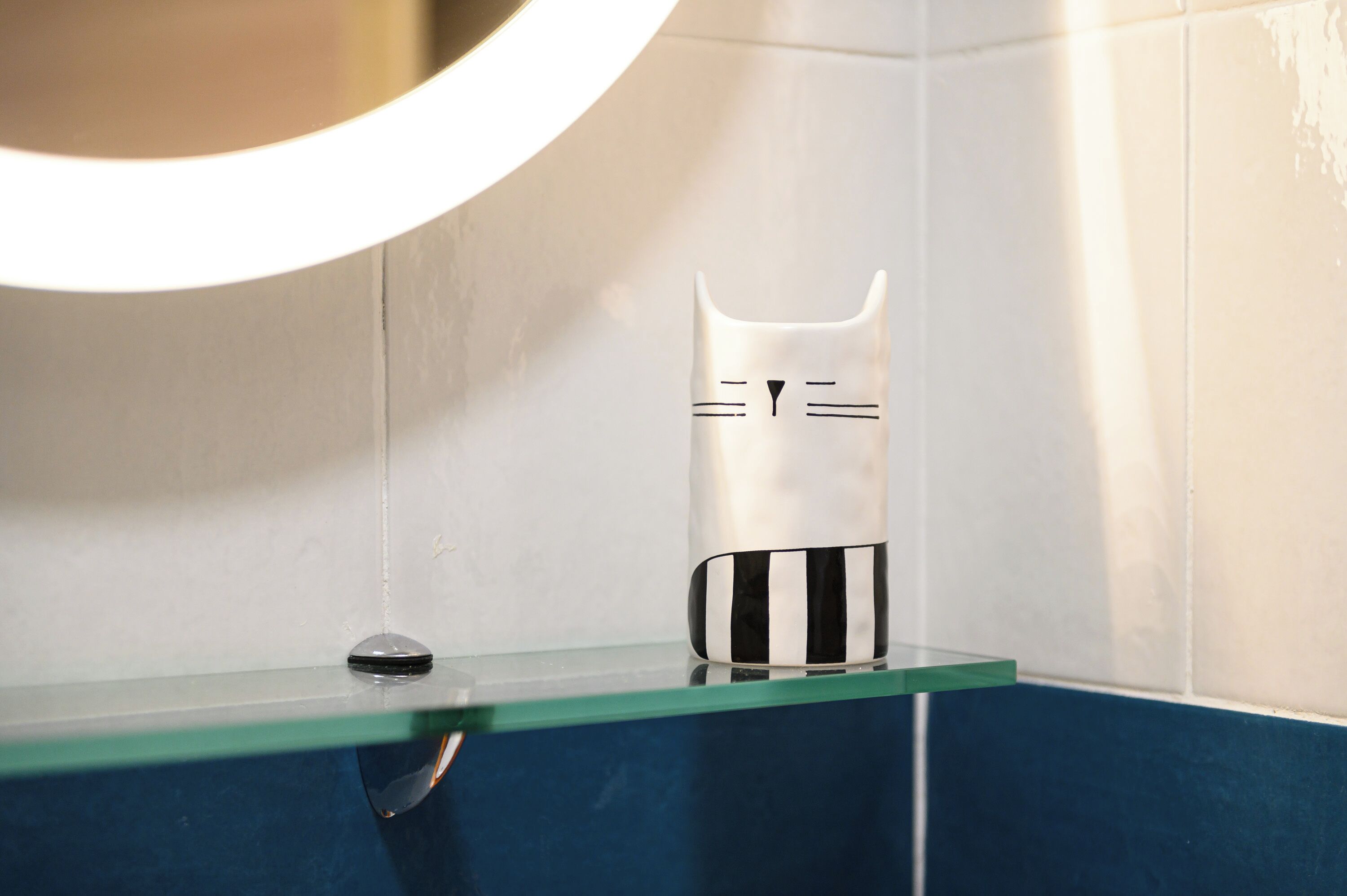 Ein Badezimmer mit einer Glasablage, auf der sich ein weißes Objekt mit schwarzen Streifen und einem Katzenmotiv befindet.