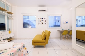 A modern, well-lit room with a sofa, a small dining table with chairs, and a TV on a stand. - L'Aurora Apartments (Naples)