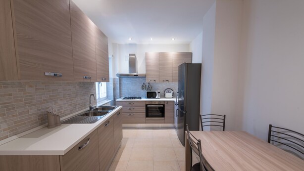 Una cocina moderna con armarios de madera, un lavamanos de acero inoxidable y una zona de comedor con mesa y sillas de madera.