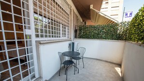 Un pequeño patio al aire libre con una mesa y sillas, una puerta blanca con diseño de celosía y un seto junto a un edificio.