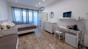 Un dormitorio con cama, escritorio, silla, refrigerador pequeño, espejo y televisión.