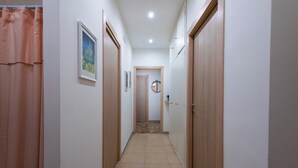 Un pasillo estrecho con puertas de madera, suelo de baldosas y un cuadro en la pared.