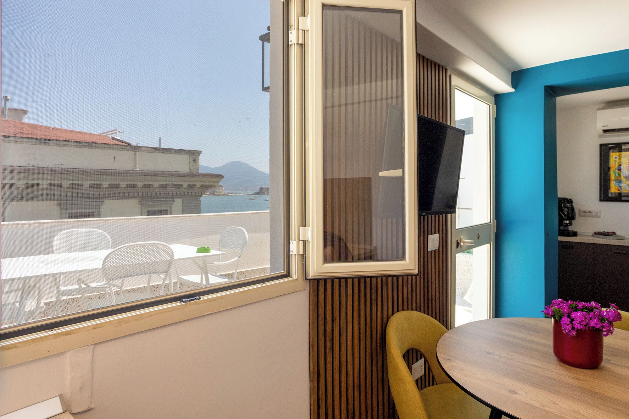 A room with a balcony, a TV, a wooden wall panel, a round table, and a chair.