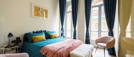 A bedroom with a bed, a chair, a bench, a lamp, and a window with curtains.