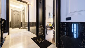 Eine Hotellobby mit Marmorboden, einer schwarzen Fußmatte mit den Buchstaben 'NA' und einer Tür zu einem Zimmer.