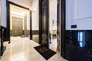 Eine Hotellobby mit Marmorboden, einer schwarzen Fußmatte mit den Buchstaben 'NA' und einer Tür zu einem Zimmer.