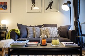 Ein modernes Wohnzimmer mit einer Couch, einem Couchtisch mit Büchern und dekorativen Objekten, einer Lampe und Kunstwerken an der Wand.