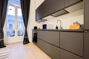 Eine moderne Küche mit dunklen Schränken, einem eingebauten Backofen und einem Fenster mit Vorhängen.