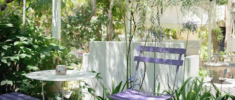 Un patio jardín con mobiliario de mimbre, una mesa con maceta decorativa y abundante follaje.