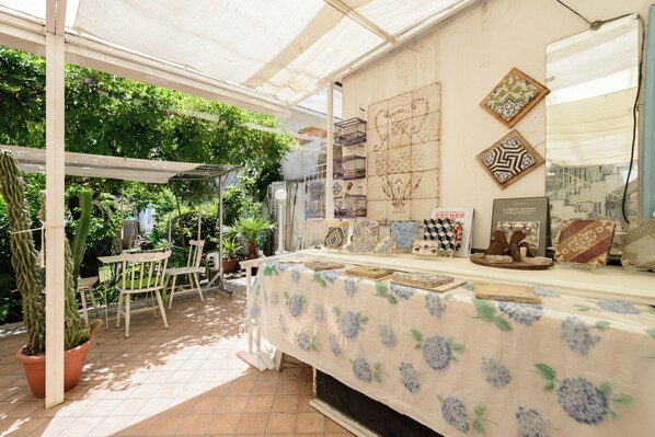 An outdoor market stall with a table covered in a floral tablecloth displaying various ceramic tiles. - Giardino Segreto - Via Foria 216 (Naples)
