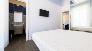 Ein Schlafzimmer mit einem großen Bett, einem an der Wand montierten Fernseher und einem Badezimmer mit Spiegel und Waschbecken.