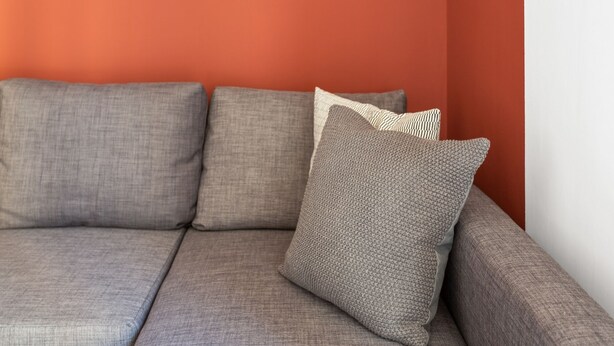 Un sofá modular con varios cojines frente a una pared roja.