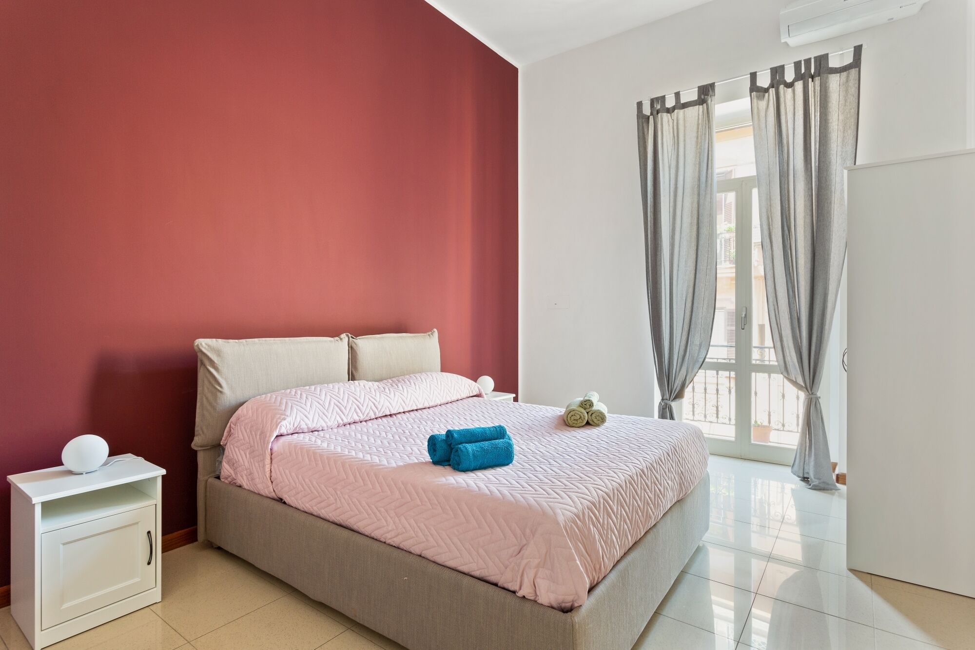 A bedroom with a bed, a nightstand, and a window with curtains.