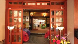 A traditional Japanese-style entrance with sliding doors, a reception area with a sofa and table, and a decorative fan.