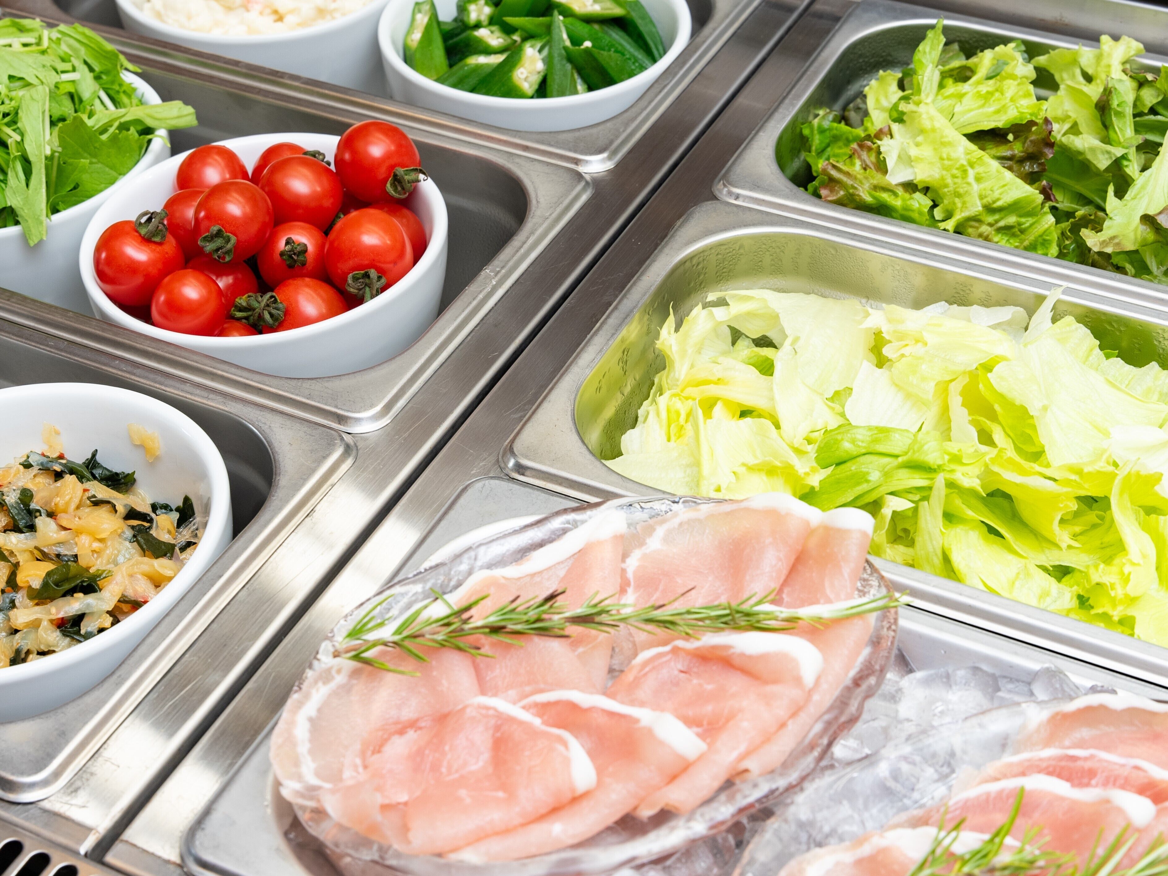 A buffet with various food options including tomatoes, lettuce, and sliced meat.