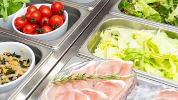 A buffet with various food options including tomatoes, lettuce, and sliced meat.