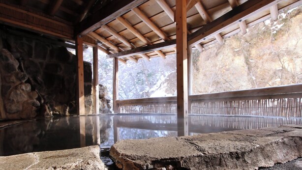 A traditional Japanese onsen with stone walls, wooden beams, and a clear view of the surrounding landscape.