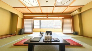 A traditional tatami room with a low table, sliding doors, and a view of trees outside.