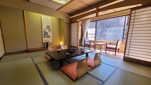 A traditional Japanese room with tatami flooring, a low table with tea set, sliding doors, and a view of trees outside.