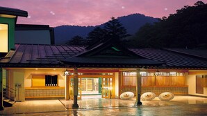 A traditional Japanese building with a tiled roof, a wooden entrance, and a view of mountains in the background.