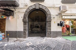 A stone archway entrance to a building with a metal gate, a sign for 'SD Blossom', and a small shop with clothes displayed outside. - Via Avvocata 25 (Naples)