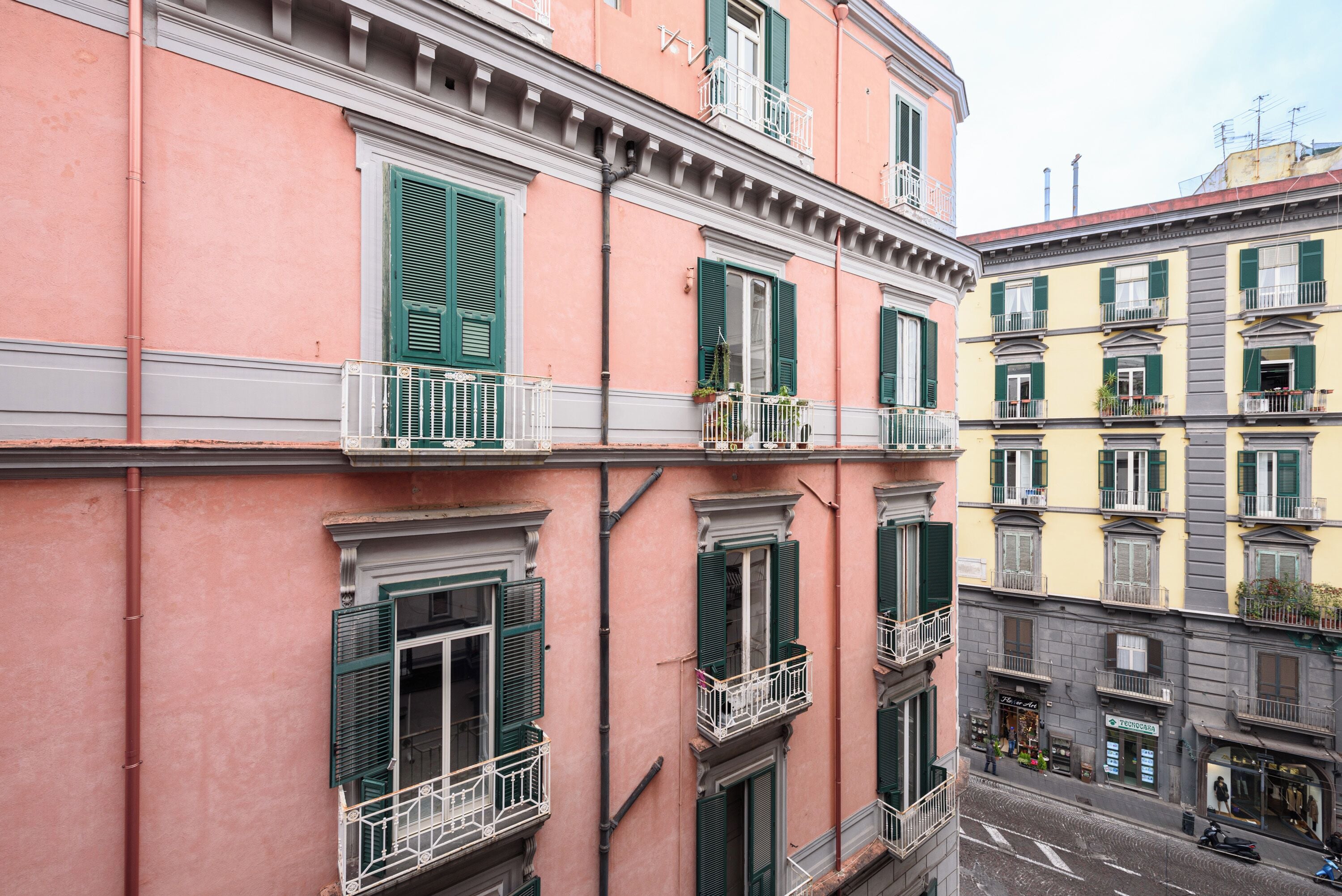 A multi-story building with balconies, green shutters, and a street view.
