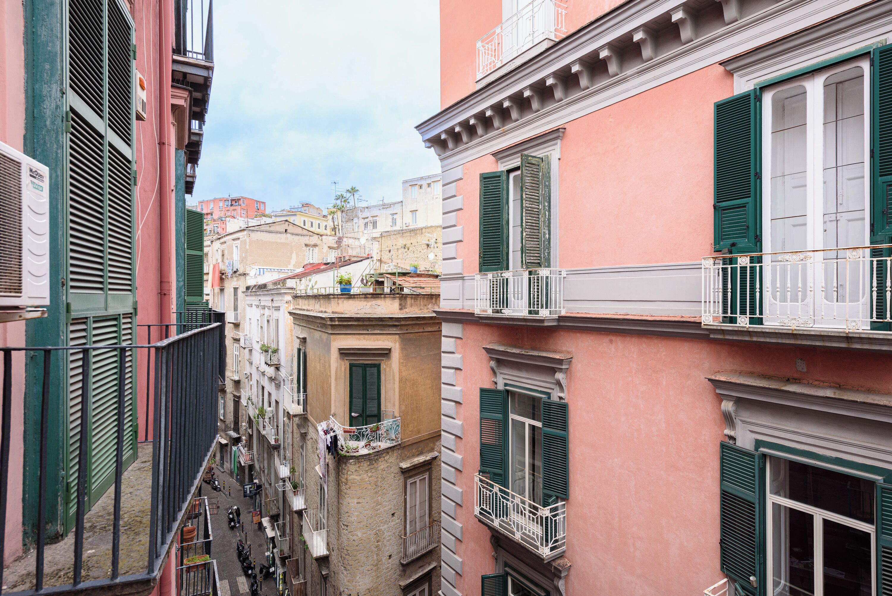 Rua estreita entre edifícios com varandas, algumas com roupa a secar.