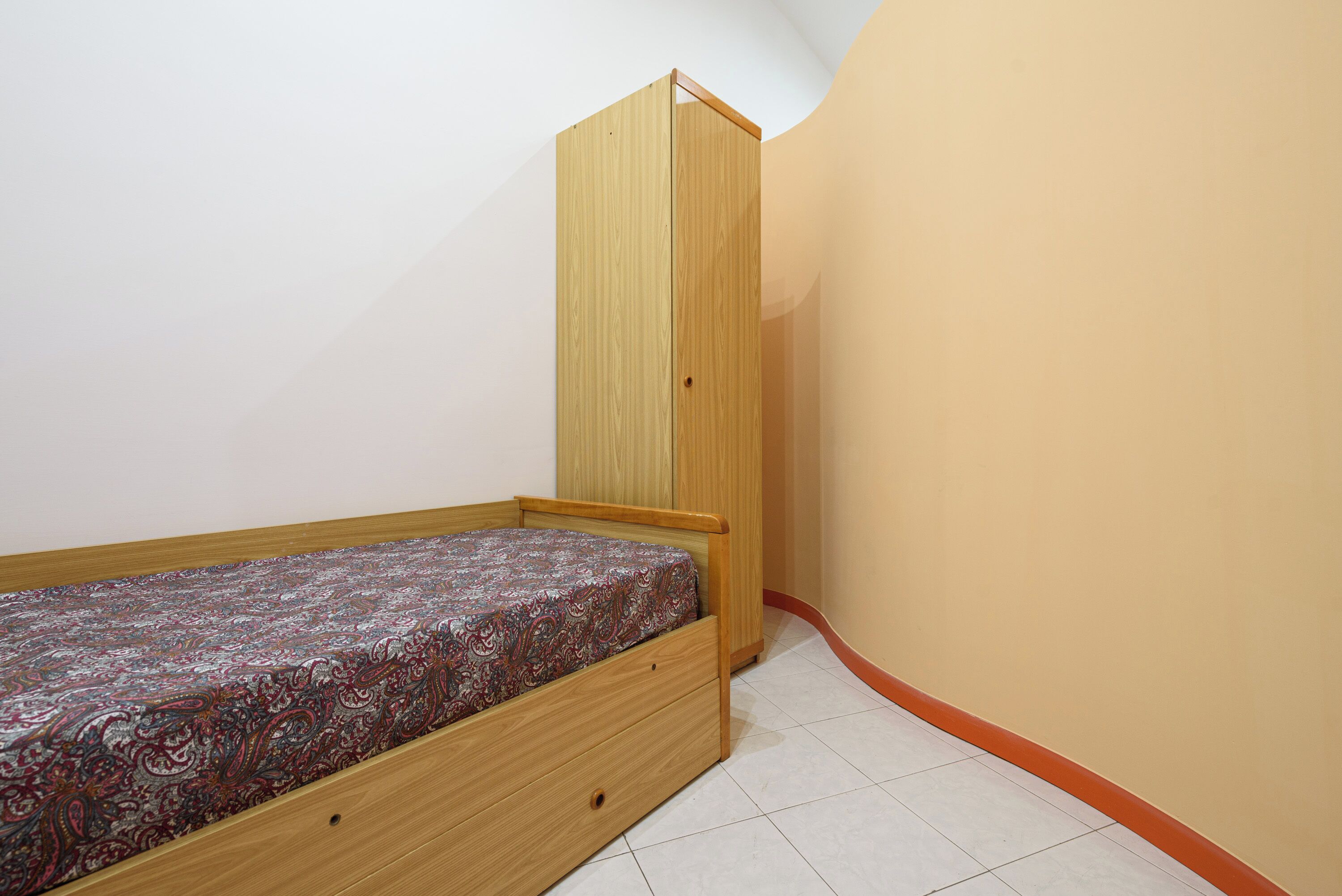 A small, single-bed room with a wooden bed frame and a built-in wardrobe.