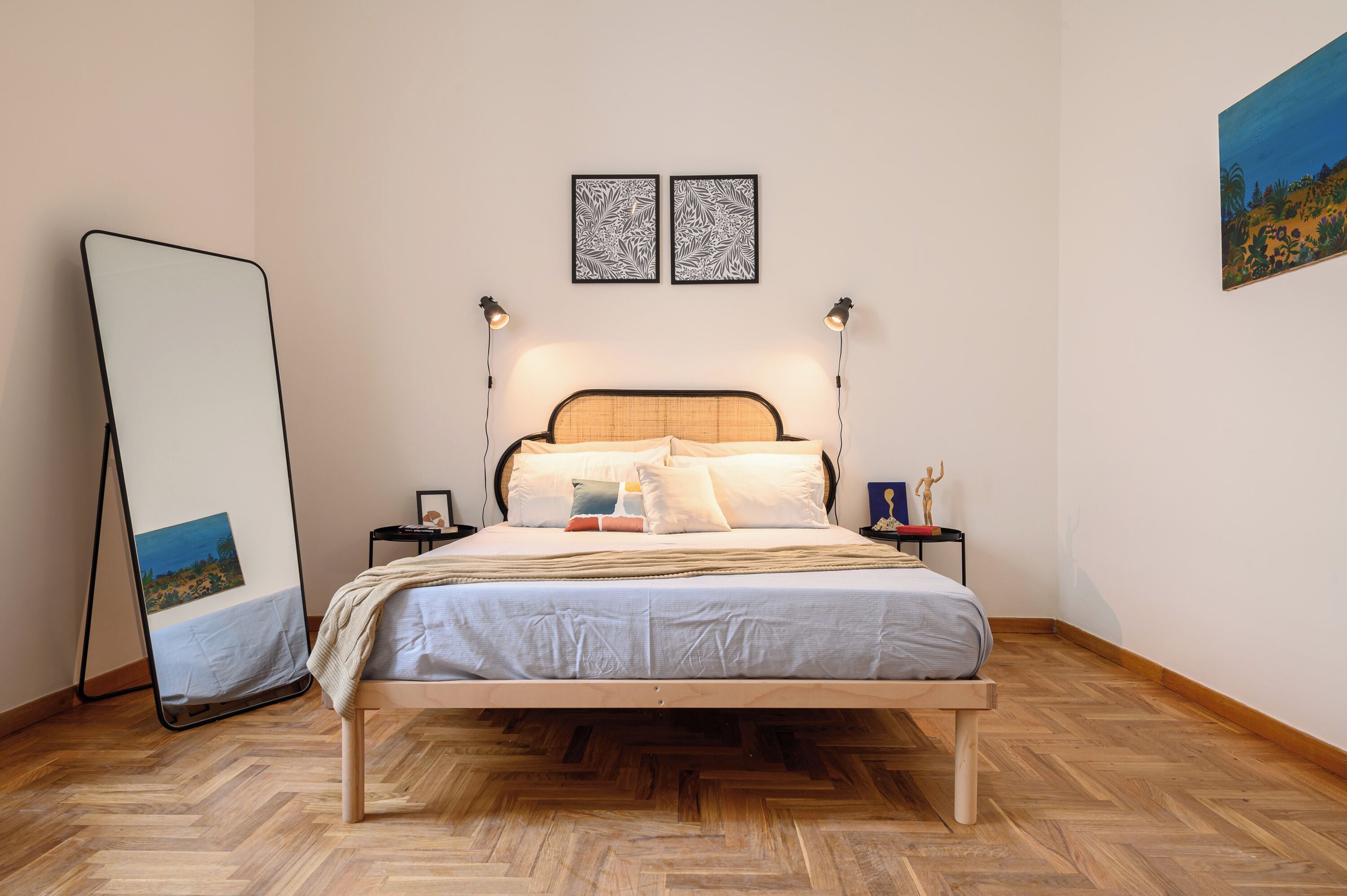 Een keurig opgemaakt slaapkamer met een houten bed, een nachtkastje met een lamp, en een grote spiegel die tegen de muur staat.