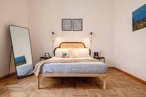 Une chambre à coucher bien rangée, avec un lit en bois, une table de chevet dotée d’une lampe et un grand miroir appuyé contre le mur.