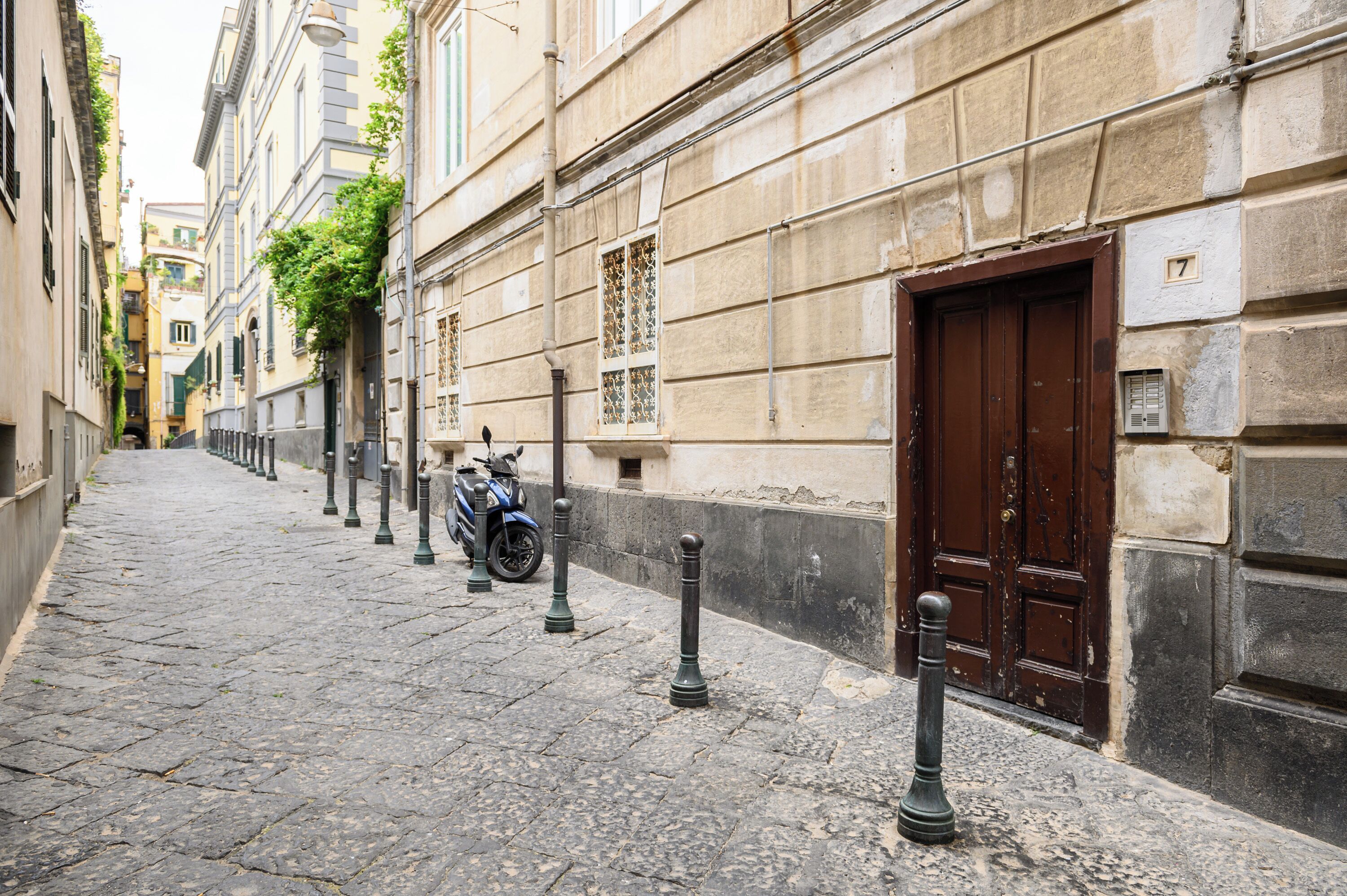 A narrow cobblestone street lined with historic buildings, a brown door, and a parked scooter.