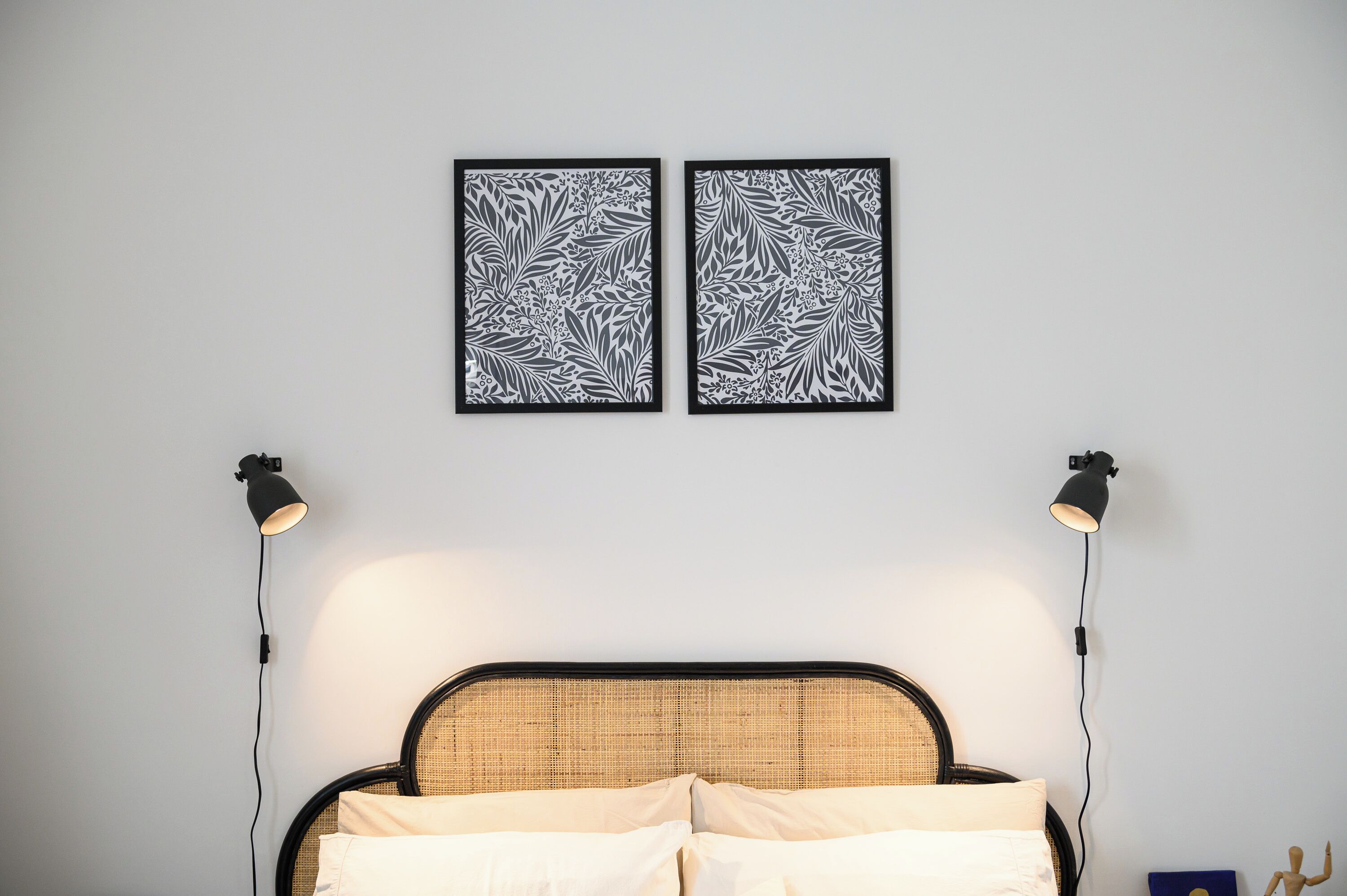 A bed with a woven headboard, two wall-mounted picture frames with a leaf pattern, and two bedside lamps.