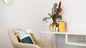 A beige armchair with a cushion, a white side table with a vase of green plants and a yellow pot, and a letter 'S' on the table. - Viale Calascione 7 (Naples)