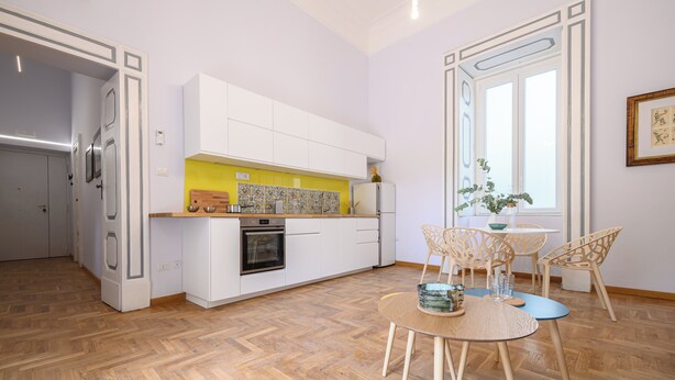 A modern kitchen with white cabinets, a yellow backsplash, and a dining area with a round table and chairs. - Viale Calascione 7 (Naples)