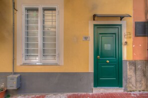 Um edifício com porta verde, janela com persianas brancas e parede amarela.