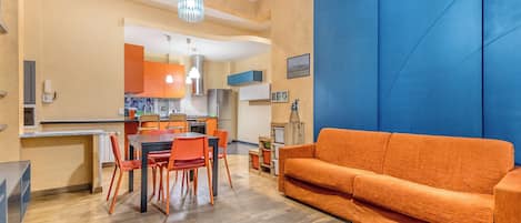 A modern living room with a sofa and dining area, kitchen in the background, and a blue accent wall.
