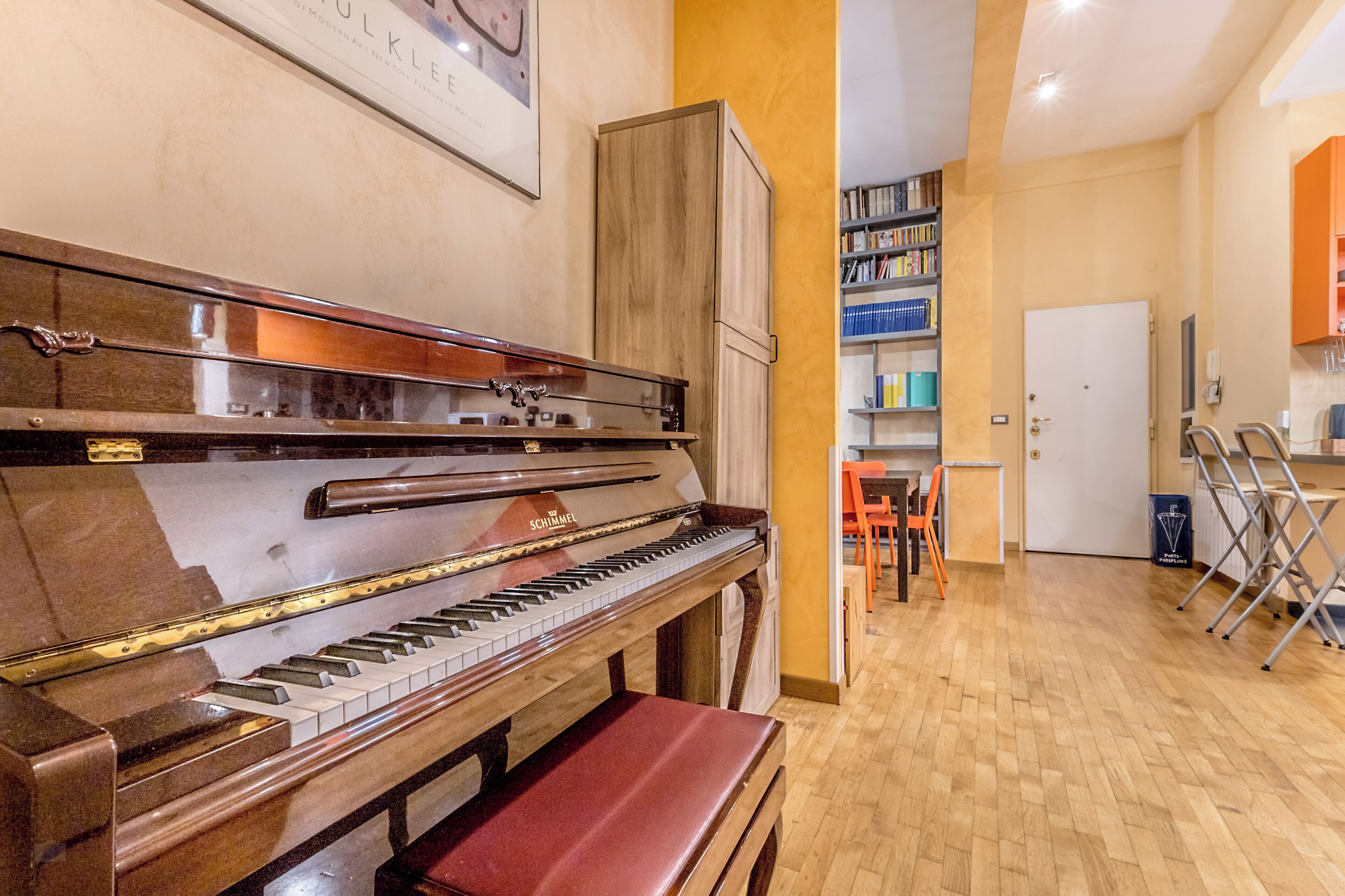 A piano in a room with wooden flooring, a bookshelf, and a door in the background.