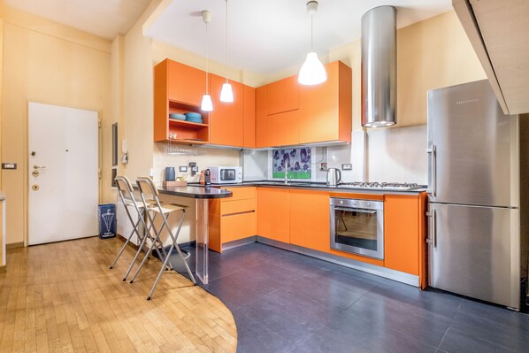 A modern kitchen with orange cabinets, stainless steel appliances, and a wooden dining area. - Il Gazebo a Monteverde (Rome)