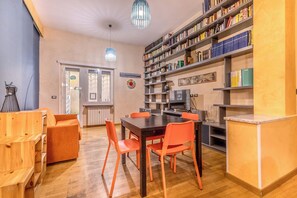 A dining area with a wooden table and orange chairs, surrounded by bookshelves and a kitchen area. - Il Gazebo a Monteverde (Rome)