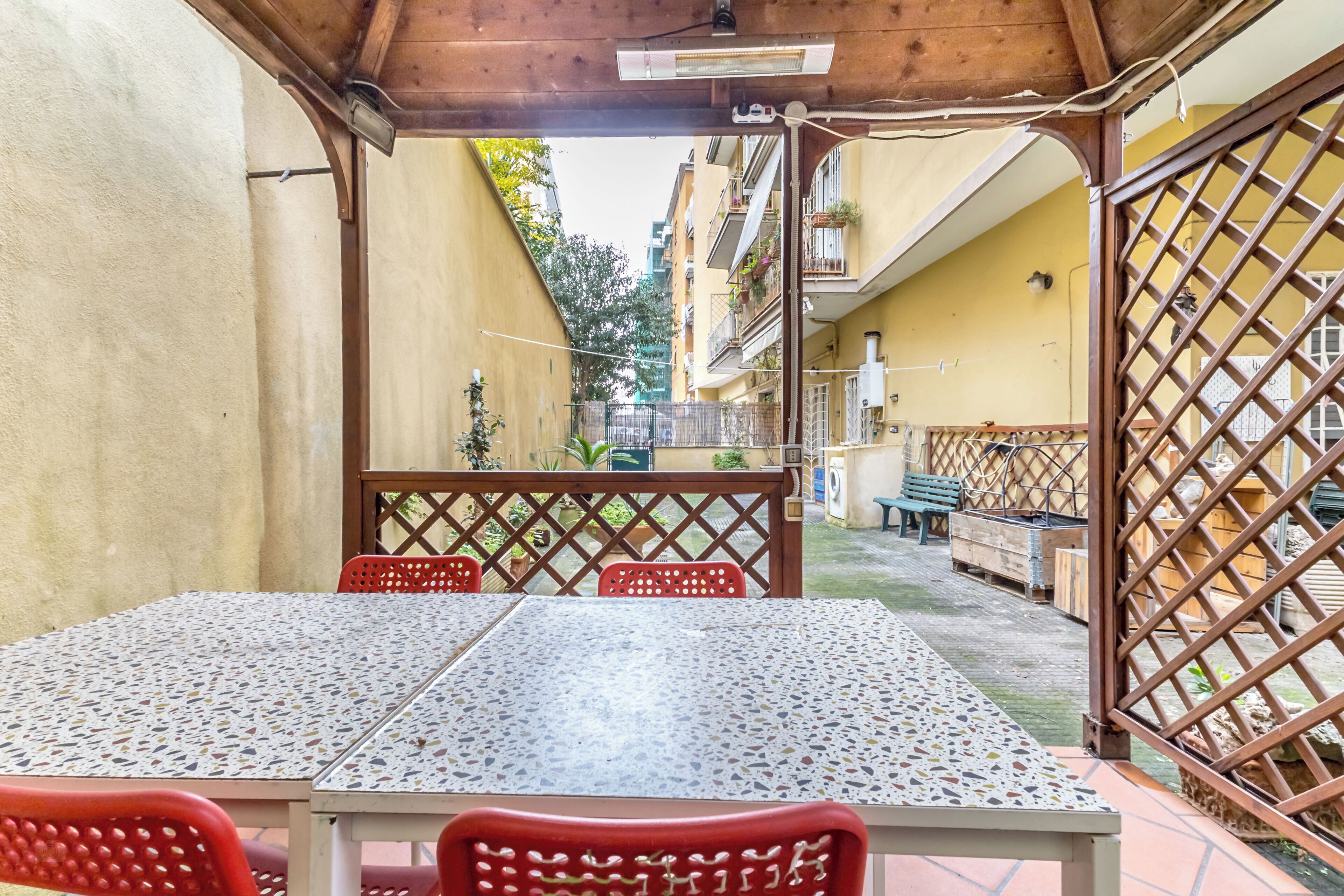 Terrassa exterior amb taula i cadires, una pèrgola de fusta i vistes als edificis circumdants.