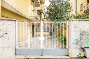 A gated entrance to a residential building with a concrete base, metal gate, and a small sign on the wall. - Il Gazebo a Monteverde (Rome)