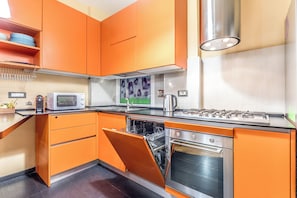 A kitchen with orange cabinets, a microwave, a stove, and a dishwasher. - Il Gazebo a Monteverde (Rome)
