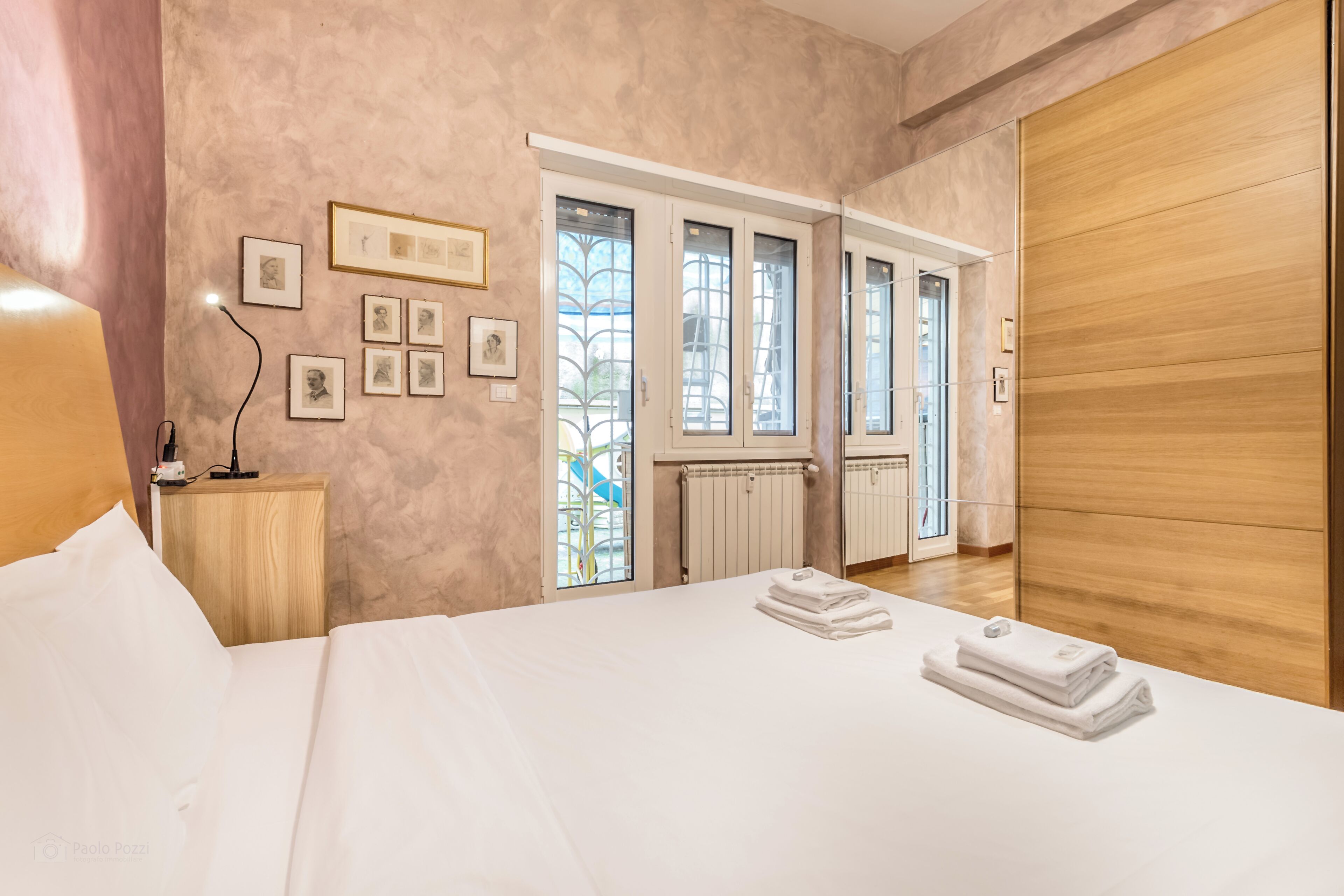 Een hotelkamer met een groot bed, een houten nachtkastje, een wandlamp en ingelijste foto's.