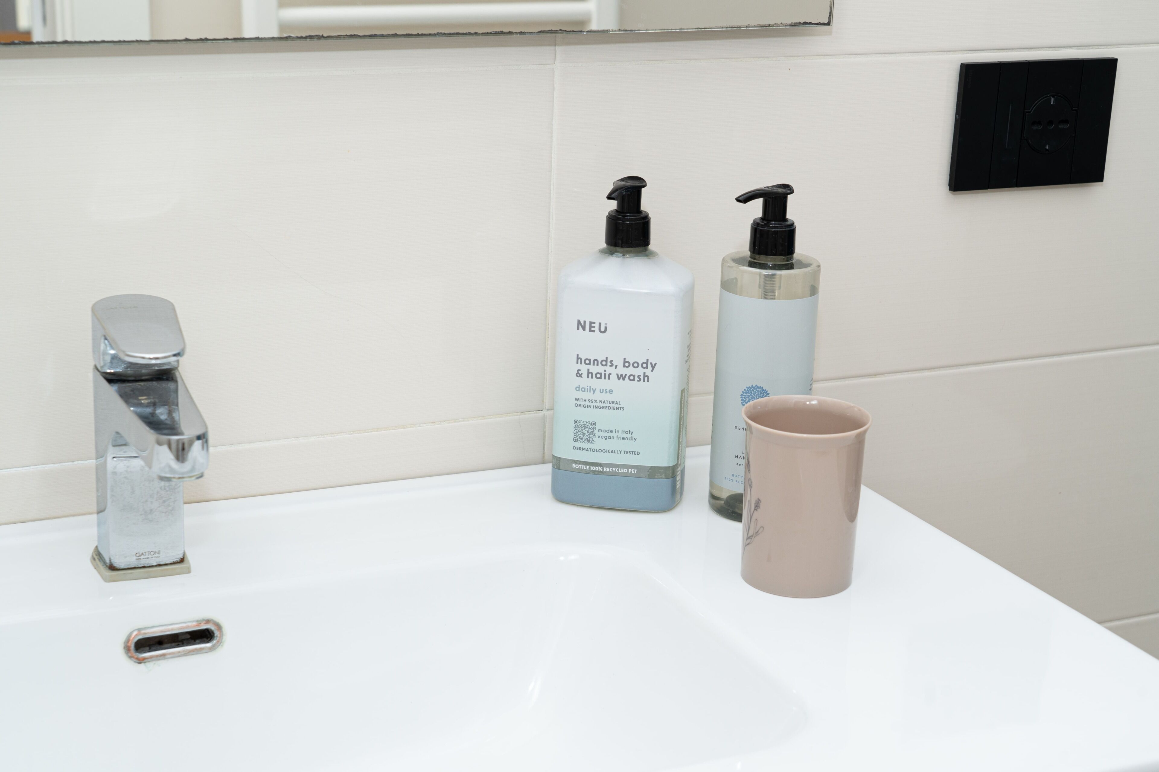 A bathroom sink with a faucet, two bottles of hand wash, and a mug.