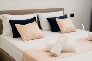 A neatly made bed with a beige bedspread, two navy blue pillows, and two beige pillows. There are two rolled towels on the bed. - Via Niccolò Tommaseo 4 - Appartamento 1 (Naples)