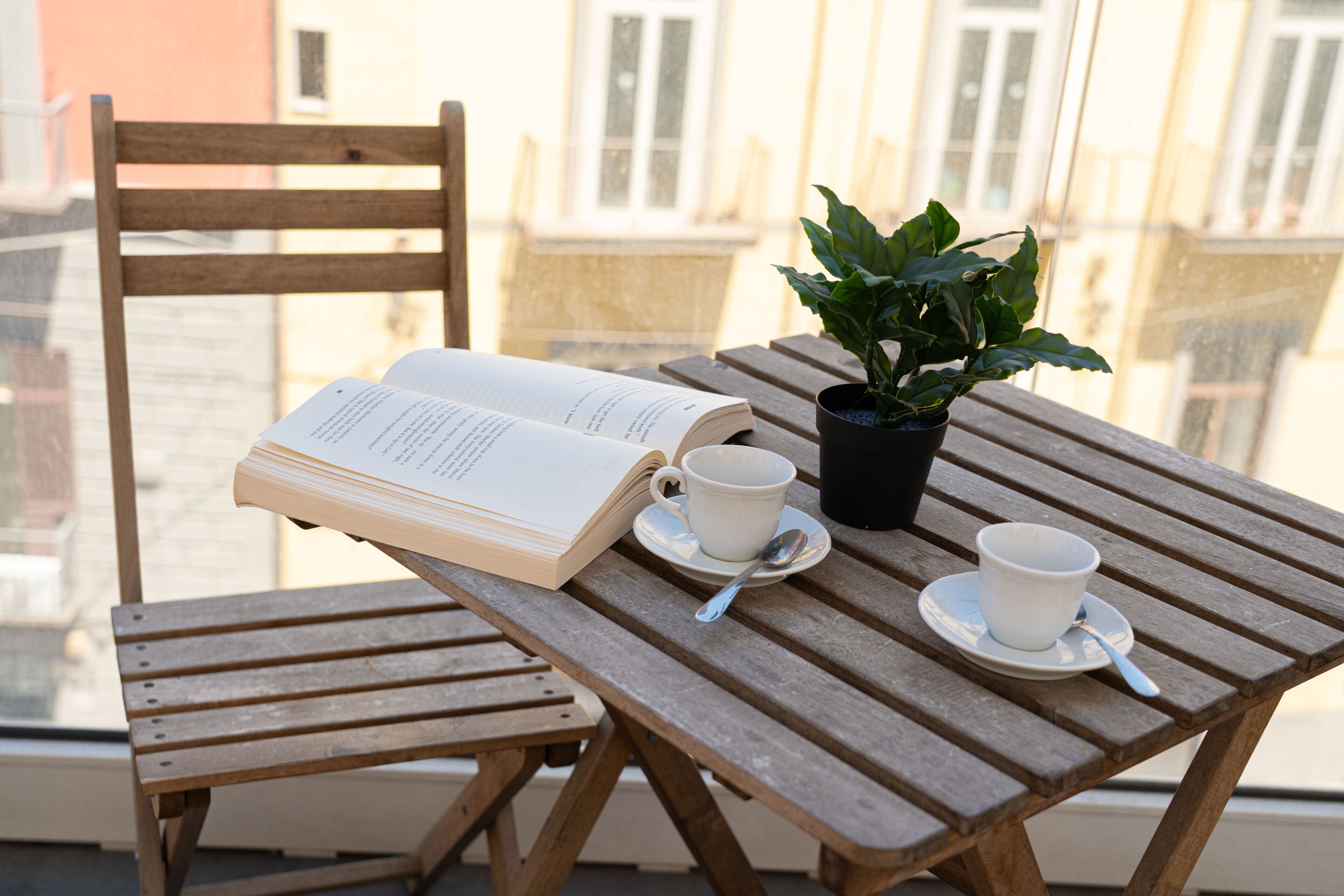 Un tavolo di legno con un libro, due tazze, un piattino e una pianta in vaso.