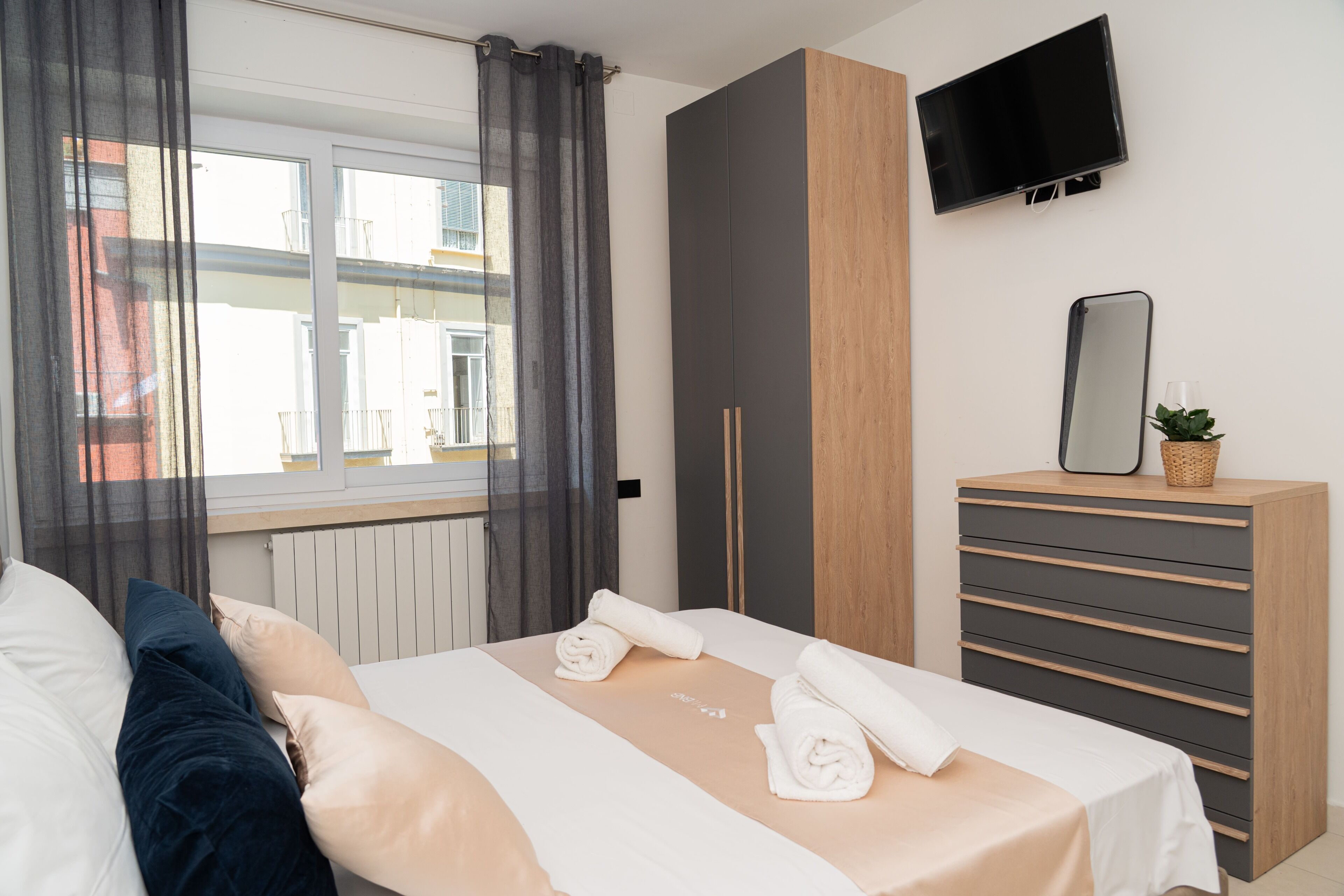 A bedroom with a bed, a dresser, a TV, and a window with curtains.