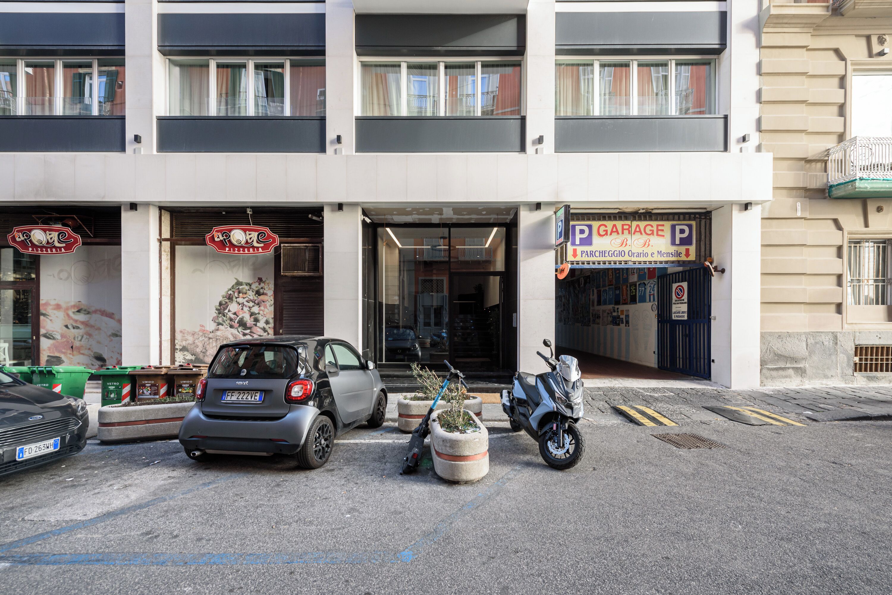 A building with a garage sign, a parked car, and a scooter.
