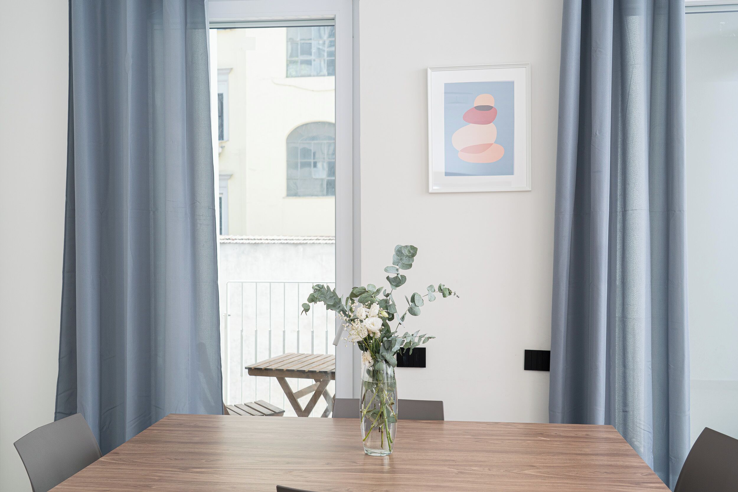 A dining area with a wooden table, grey curtains, and a framed picture on the wall.