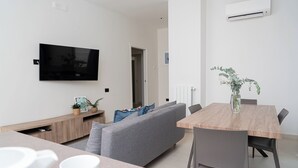 Un soggiorno moderno con televisore a schermo piatto, divano grigio, tavolo da pranzo in legno e una piccola pianta in vaso.